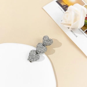 Pince à cheveux cœur argentée scintillante avec strass présentée sur une assiette blanche