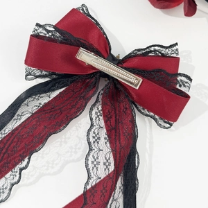Detailed view of the red satin bow hair clip with black floral lace and metal duckbill clip
