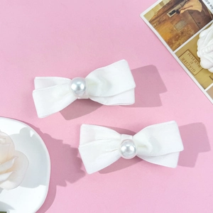 Detail of pair of white velvet bow hair clips with central pearl on pink background
