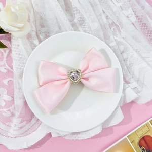 Detailed macro view of pink satin bow hair clip with rhinestone heart and pearl center