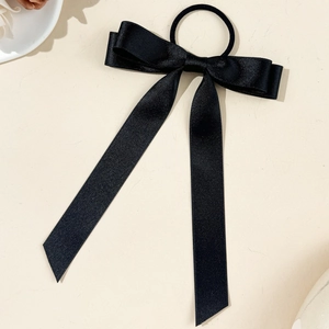Close-up of elegant black satin ribbon bow hair tie with long streamers on stone surface