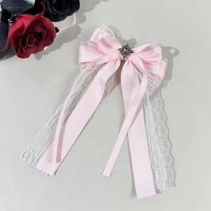 Close-up of pink satin bow hair clip with white lace, black cameo, and long tassels