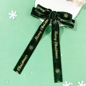 Close-up of dark green velvet bow clip with gold Merry Christmas print and star pattern