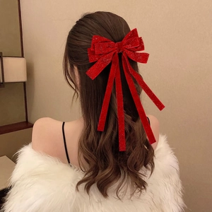 Detail of red velvet bow hair clip with silver glitter and long streaming ribbons