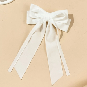 Close-up of elegant white satin bow hair clip with long flowing ribbons on neutral base