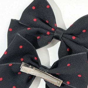 Detail of black ribbon bow hair clip with red polka dots and silver metal duckbill clip