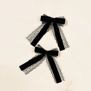 Detailed macro view of two-piece black velvet and lace bow hair clips with long ribbons