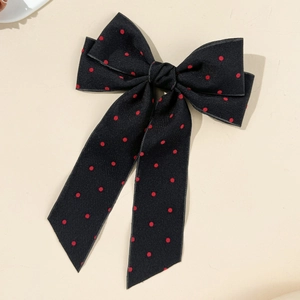 Detailed view of large black textured fabric bow hair clip with red polka dots and long ribbons