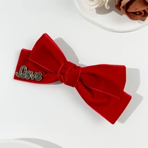 Detail view of red velvet bow hair clip featuring a golden Love metal letter accent