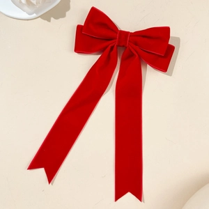 Macro view of red velvet bow hair clip with long streamers on beige textured surface