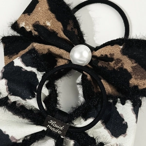 Macro detail of leopard print bow hair scrunchie with white pearl and handmade label