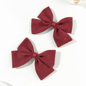 Close-up of two elegant burgundy polka dot bow hair clips with twill fabric texture