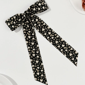 Detail of a large black bow hair clip with leopard heart print and long flowing streamers