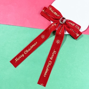 Close-up of red velvet Christmas bow hair clip with gold Merry Christmas print and gemstone