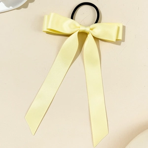 Detail of light yellow satin bow hair tie with long ribbons on a neutral background