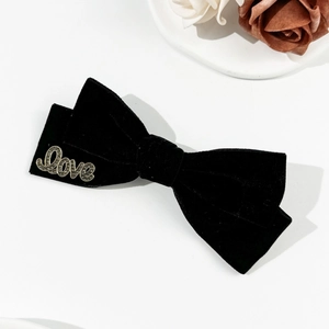Detail of black velvet bow hair clip featuring a gold-toned Love letter metal ornament