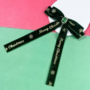 Detail of green velvet Christmas bow clip with emerald gem and gold Merry Christmas text
