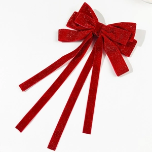 Macro detail of the red velvet hair clip with glitter finish and long flowing ribbons