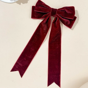 Detail of burgundy velvet bow hair clip with long ribbons on a plain background