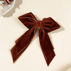 Close-up of elegant dark brown velvet bow hair clip with ribbons on beige background
