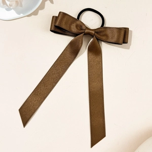 Detailed view of dark brown silk bow hair tie with long ribbons on a textured surface