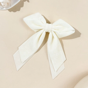 Close-up of elegant white velvet bow hair clip with long ribbons on beige background