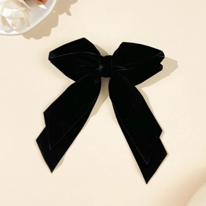 Detail view of a black velvet double-layered bow hair clip with ribbons on beige backdrop