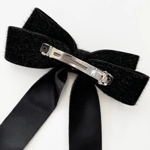 Detail of black plush bow hair clip with satin ribbons and silver spring fastener