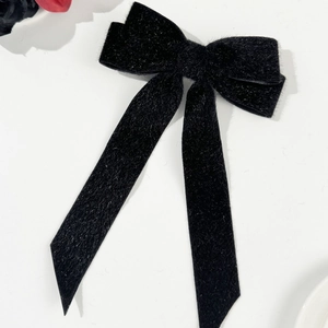 Detail view of a black velvet bow hair clip with shimmering glitter and long ribbons