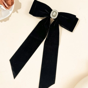 Elegant black velvet bow hair clip with vintage rhinestone center on a beige background