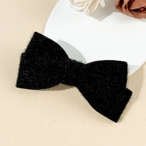 Close-up of black plush bow hair clip with sparkling silver threads on a white plate