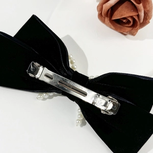 Macro shot of the silver metal spring clip and pearl-edged black velvet bow hair clip