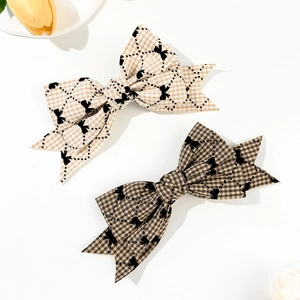 Détail de pinces à cheveux à carreaux abricot et marron avec motifs de petits nœuds noirs
