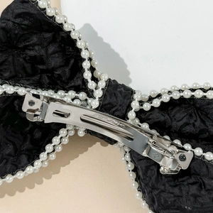 Detail of elegant black bow hair clip featuring faux pearl trim and silver metal spring clip