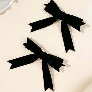 Detail showing the rich texture of pair of black velvet bow hair clips on white surface