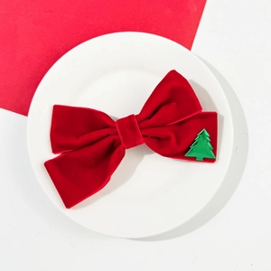 Detail of red velvet Christmas bow with a small green holiday tree and golden bell