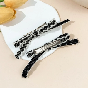Detail showing two plush black bow hair clips with white trim on a white plate