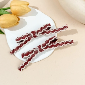 Detail showing two wine red bow hair clips with white stitching on a ceramic plate