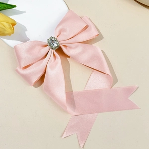 Close-up of pink satin bow hair clip with luxury crystal centerpiece and long ribbons