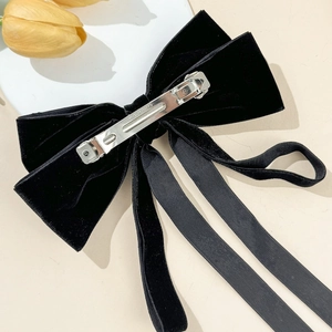 Detail shot of black velvet bow hair clip showing the metal spring clip with engraved text
