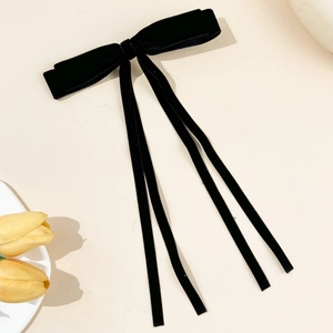 Close-up of a premium black velvet double bow hair clip with long streamers on beige background
