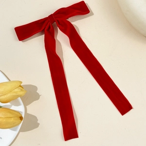 Elegant red velvet bow hair clip with long streamers on a beige textured background