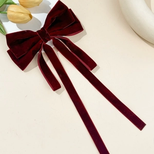 Detail of burgundy velvet bow hair clip with long ribbons on a warm aesthetic background