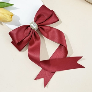 Detail of burgundy satin bow hair clip featuring a large square rhinestone and ribbon tails