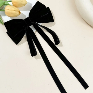 Detailed view of black velvet bow hair clip with long ribbons on a beige background