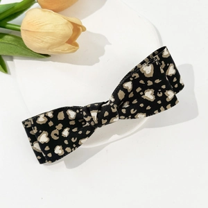 Leopard print bow hair clip with heart patterns on a white display board with tulips