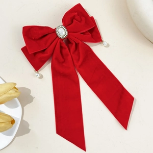 Close-up of a red velvet bow hair clip with central pearl and golden filigree detail