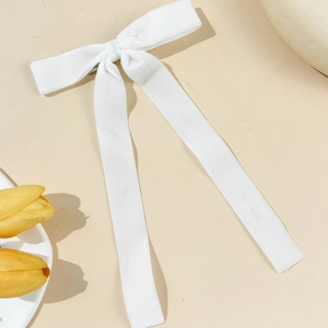Detail view of a white velvet bow hair clip with long ribbons on a minimalist background