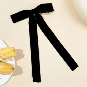 Detailed view of an elegant black velvet bow hair clip with long ribbons on a beige surface