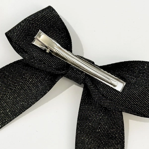 Macro view of black bow hair clip with gold thread details and silver metal alligator clip